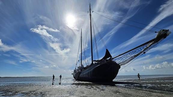 Tjalk Aagtje drooggevallen op het Wad met mensen naast het schip