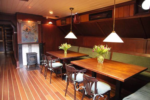 Salon van de Aldebaran met houten eettafels en rode zitbanken