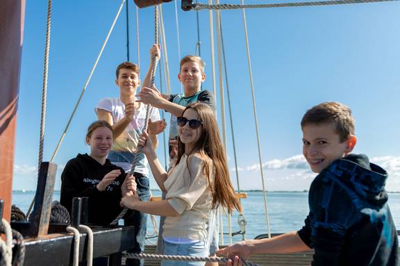 Scholieren helpen met zeilen aan boord van de Ambiance
