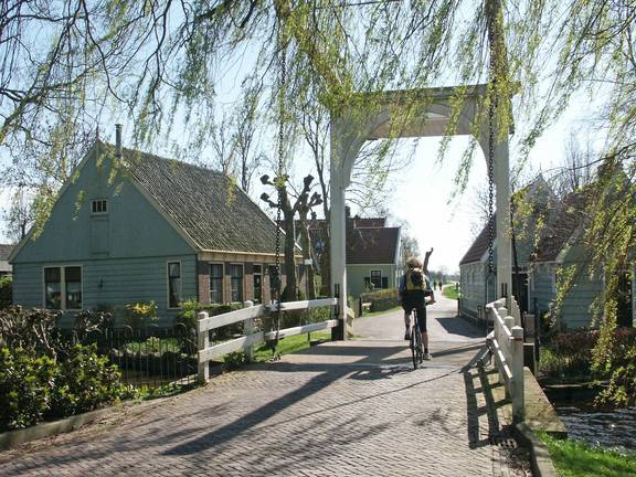 Fietser op een ophaalbrug tussen houten huizen en treurwilgen