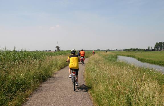 Fietsers op een fietspad door de polder, met een molen in de verte