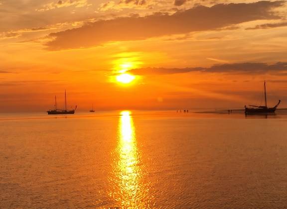 Oranje zonsondergang boven het water met zeilschepen aan de horizon