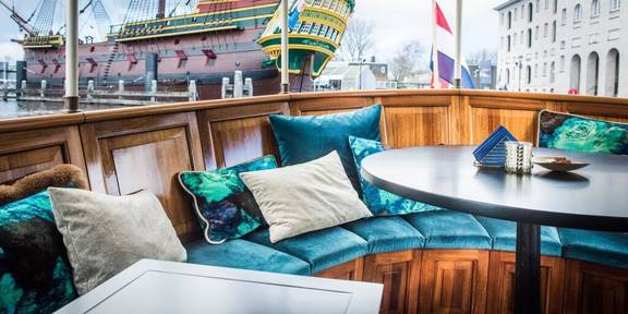 Zithoek met turquoise kussens op het achterdek van de Dame van Amstel