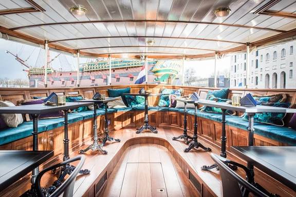 Lichte salon van de Dame van Amstel met houten tafels en turquoise zitbanken