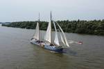 De Hester onder zeil met een bijboot naast het schip