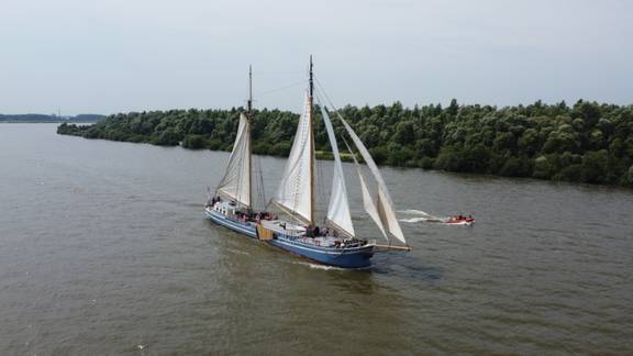De Hester onder zeil met een bijboot naast het schip