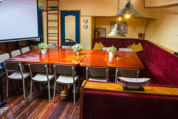 Salon van de Gouwzee met houten eettafels en rode zitbanken