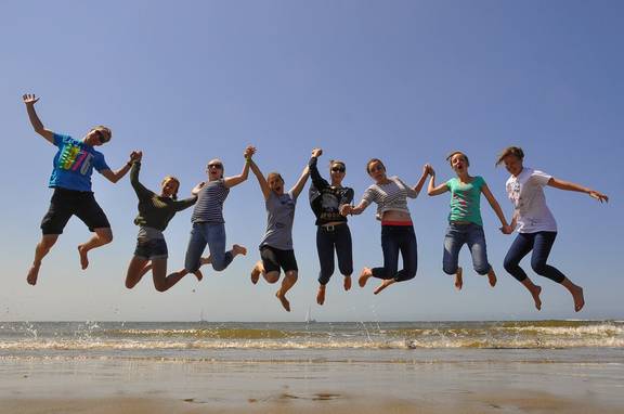 Groep scholieren springt samen omhoog op het strand