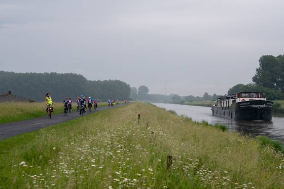 Fietsgroep op de dijk langs een kanaal, met het passagiersschip Magnifique III