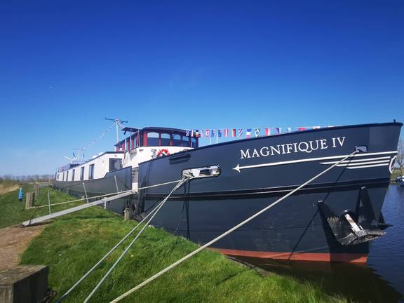 Het passagiersschip Magnifique IV aangemeerd aan een grasoever