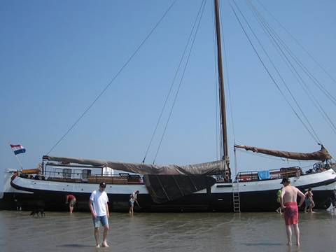 Tjalk Nieuwe Zorg drooggevallen op het Wad met gasten naast het schip