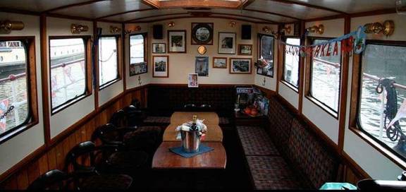 Houten salon met zitbanken en tafels aan boord van de Oude Maze