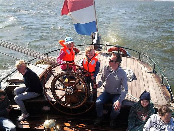 Gasten bij het stuurwiel op het achterdek van de Pelikaan