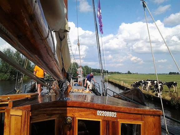 Uitzicht over het dek van de Pelikaan langs een groene oever