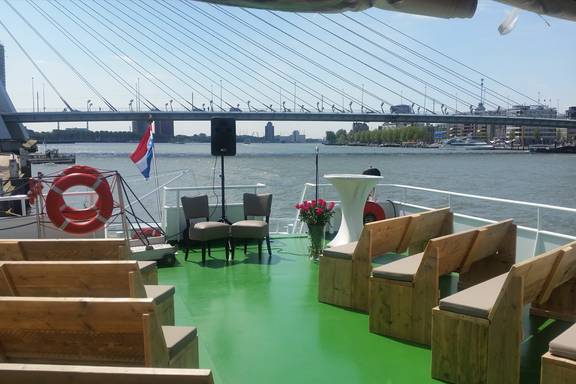Houten banken op het groene dek van de Smaragd 1 met uitzicht op de Erasmusbrug
