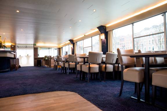 Ruime salon van de Smaragd 2 met tafels en stoelen langs de ramen