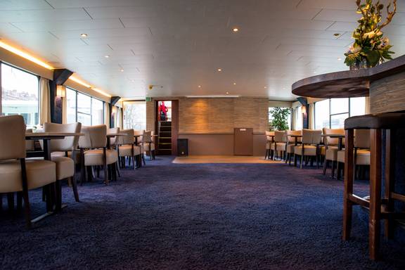Ruime salon van de Smaragd 2 met tafels en stoelen langs de ramen