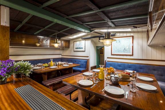 Houten salon van de Spes Mea met gedekte tafels en blauwe zitbanken