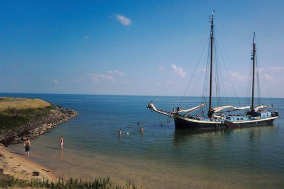 Sybaris ligt voor anker naast een zandige oever