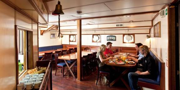 Gasten aan de eettafels in de houten salon van de Thalassa