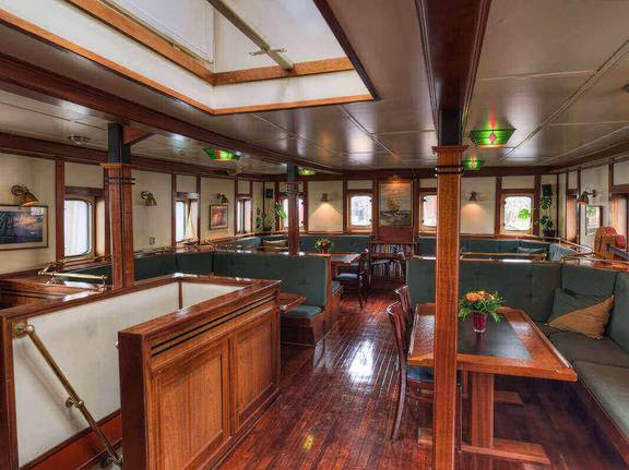 Houten salon van de Thalassa met tafels en groene zitbanken