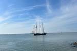 Driemaster Vrijheid zeilt op kalm water langs de kust
