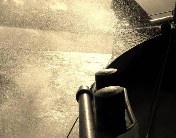 Opspattend water naast de romp van De Vrouw Dina tijdens het zeilen