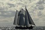 Klipper Waterman onder zeil op glinsterend water onder donkere wolken