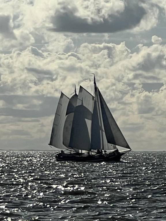Klipper Waterman onder zeil op glinsterend water onder donkere wolken