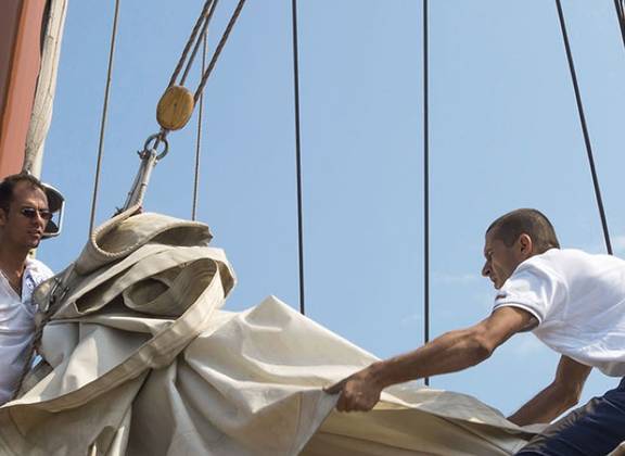 Gasten bedienen samen de zeilen aan dek van een zeilschip