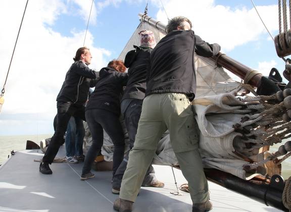 Gasten aan dek bij het stuurwiel van een zeilschip