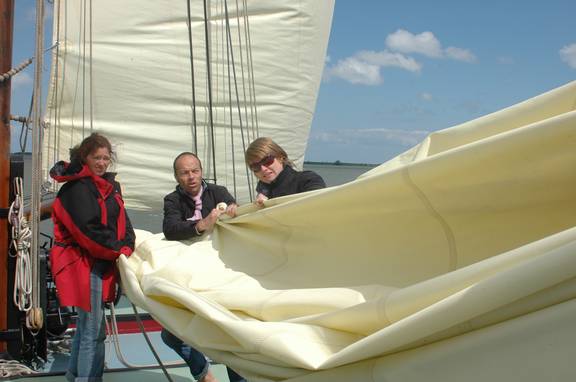 Gasten vouwen samen een zeil op aan dek van de Gulden Belofte