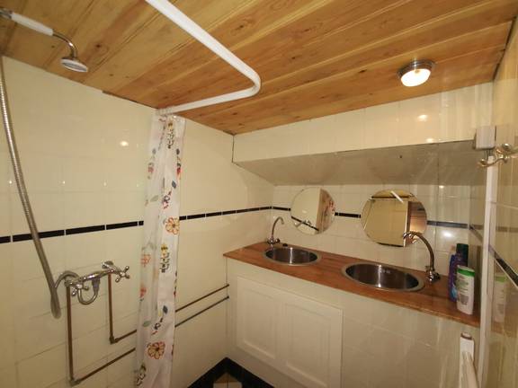 Badkamer van De Lis met wastafel en douche onder een houten plafond