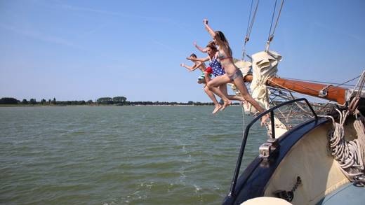 Scholieren springen vanaf een zeilschip het water in