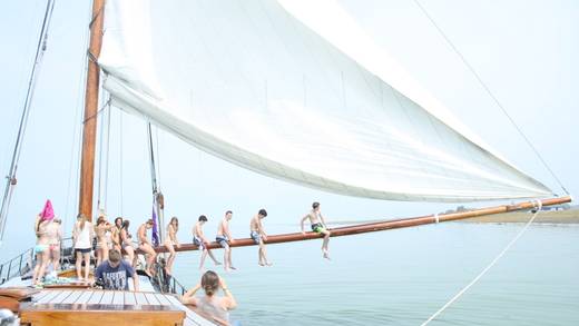 Scholieren balanceren samen op de giek van een zeilschip