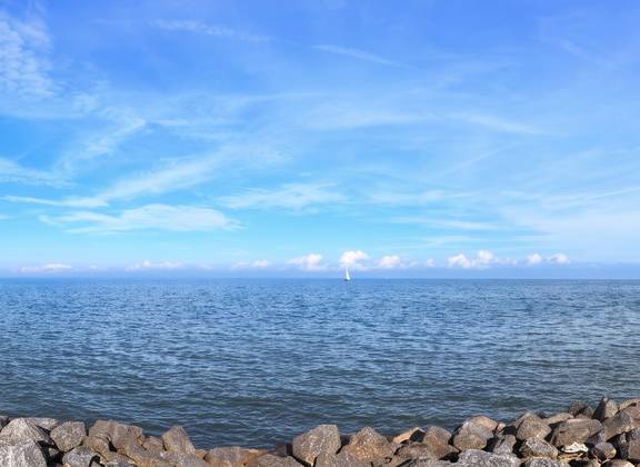 Uitzicht over het IJsselmeer langs een stenen oever en vuurtoren