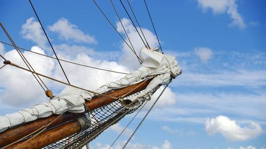 Uitzicht omhoog langs een mast met witte zeilen en tuigage
